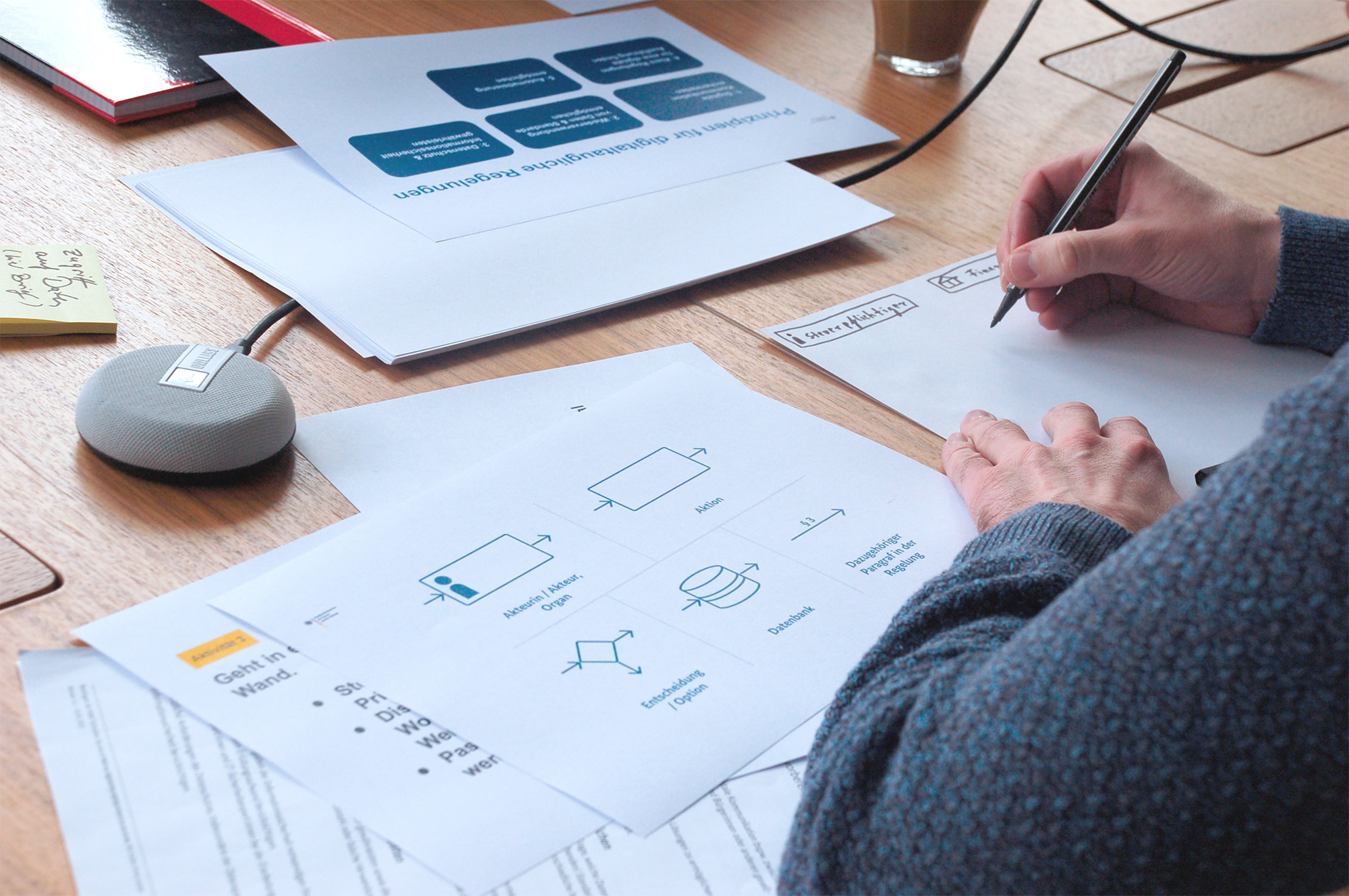 Eine Person sitz an einem Tisch und schreibt auf ein Papier. Vor ihr liegt ein Blatt, das unterschiedliche Symbole anzeigt.