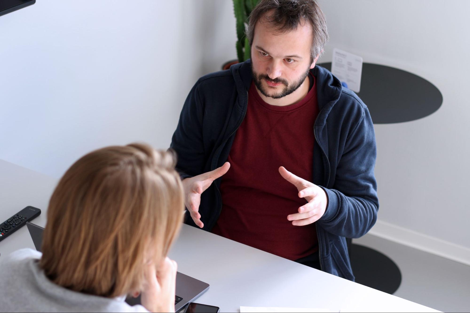 Benjamin im Gespräch mit dem Interviewer; die beiden sitzen an einem Tisch und Benjamin gestikuliert mit den Händen, um etwas zu erklären