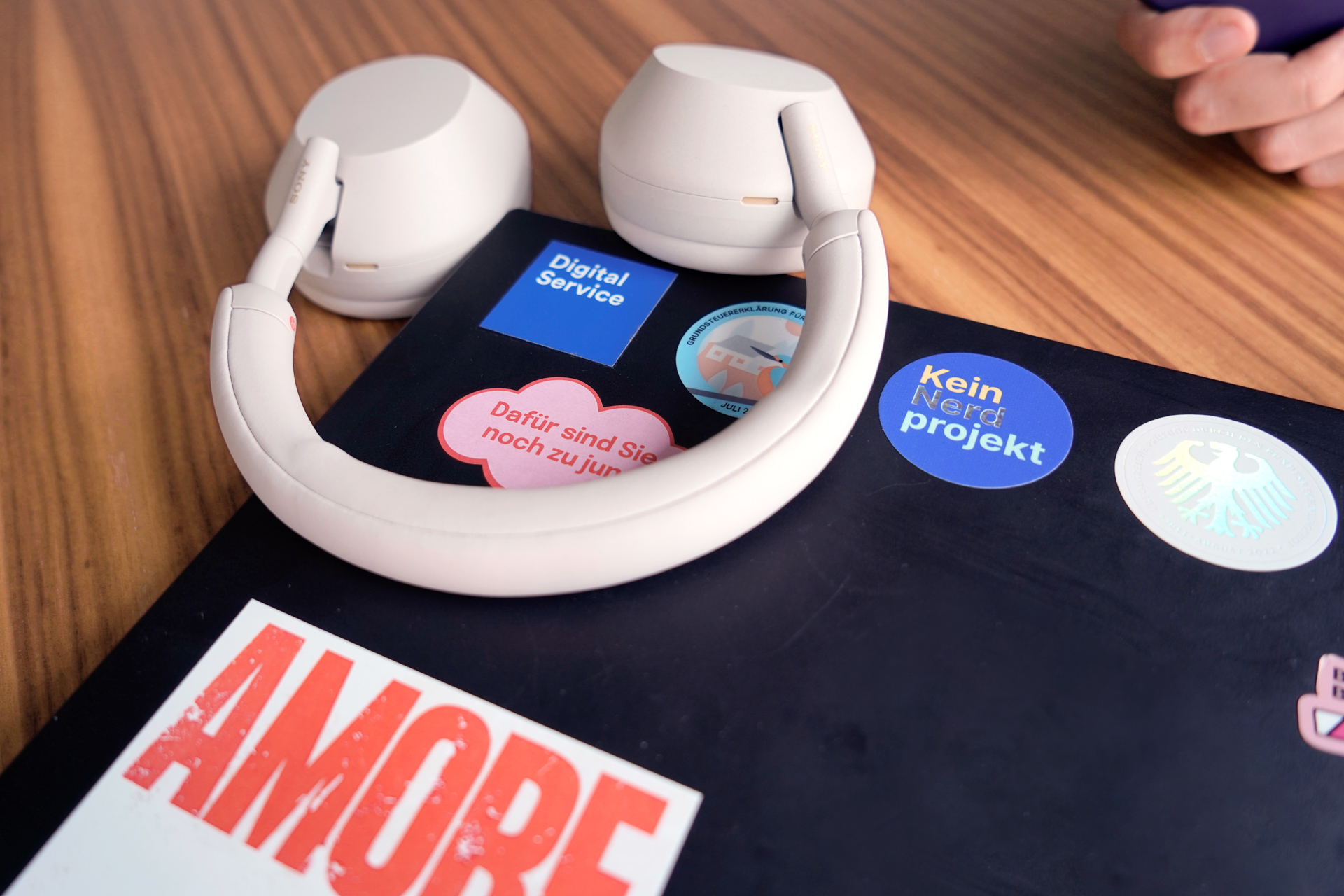 Lisas Köpfhörer und ihr Laptop, auf dem verschiedene Sticker zu sehen sind, auf einem Bürotisch in Nahaufnahme