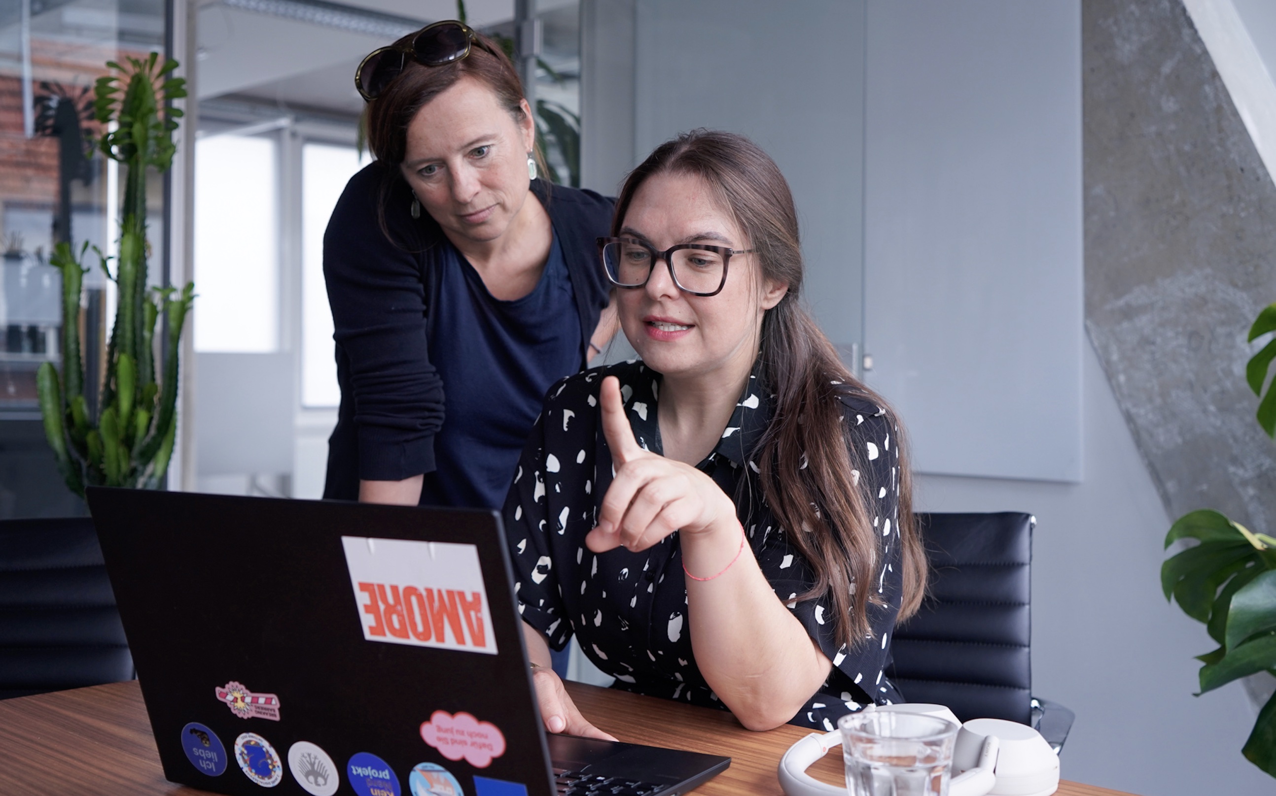 Interviewpartnerin Lisa im Gespräch mit einer Kollegin; beide schauen in das Laptop von Lisa und diese erklärt, was auf dem Bildschirm zu sehen ist