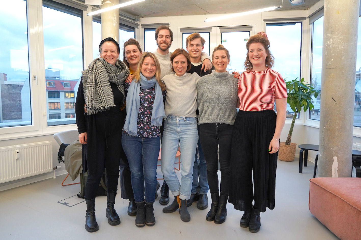 Das Fellowship-Team von Work4Germany posiert fröhlich in einem hellen Büroräum; das Team besteht aus acht Personen