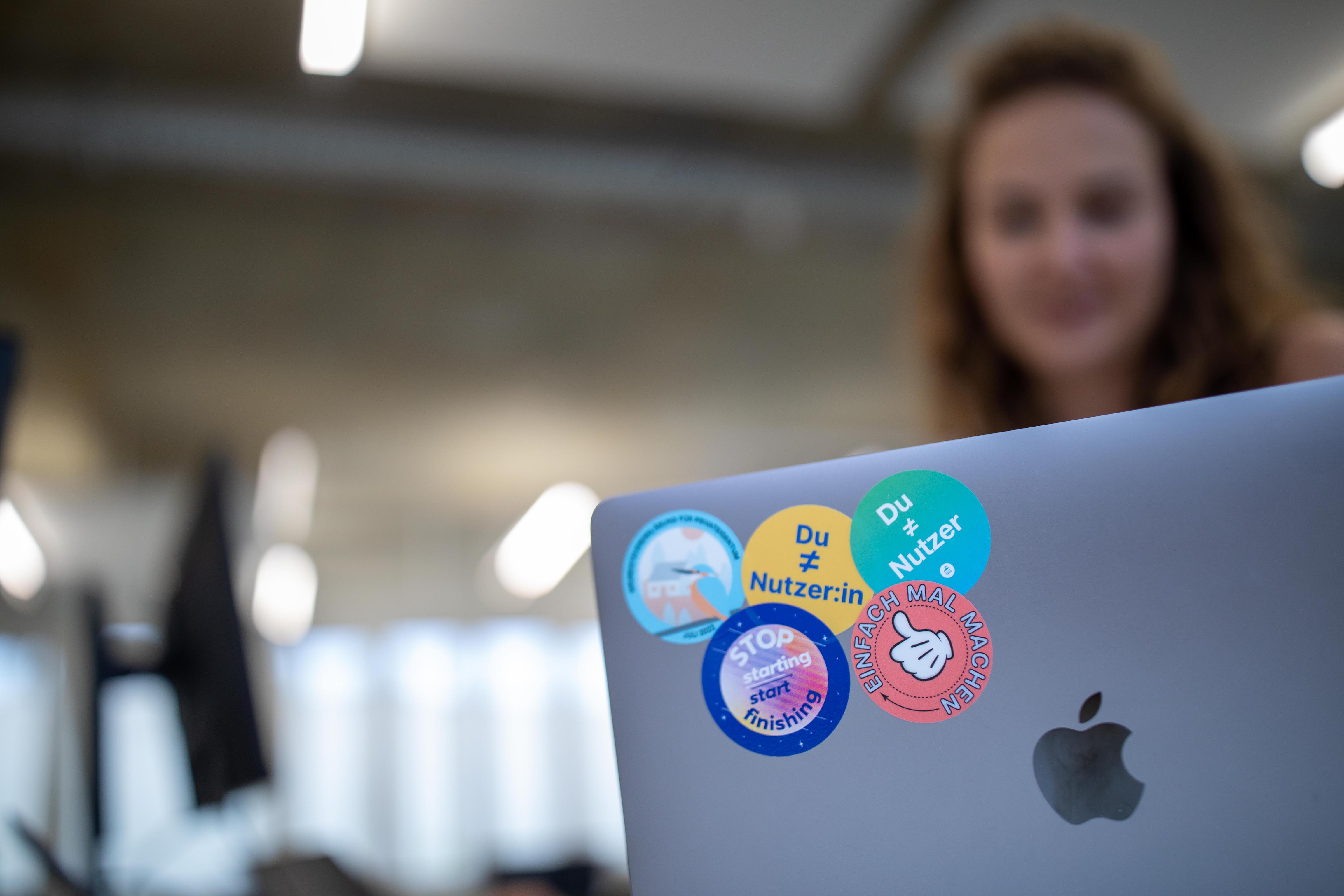 Auf der Rückseite eines Laptops sind mehrere Sticker mit verschiedenen Slogans zu sehen; auf einem der Sticker steht „Du ≠ Nutzer:in“