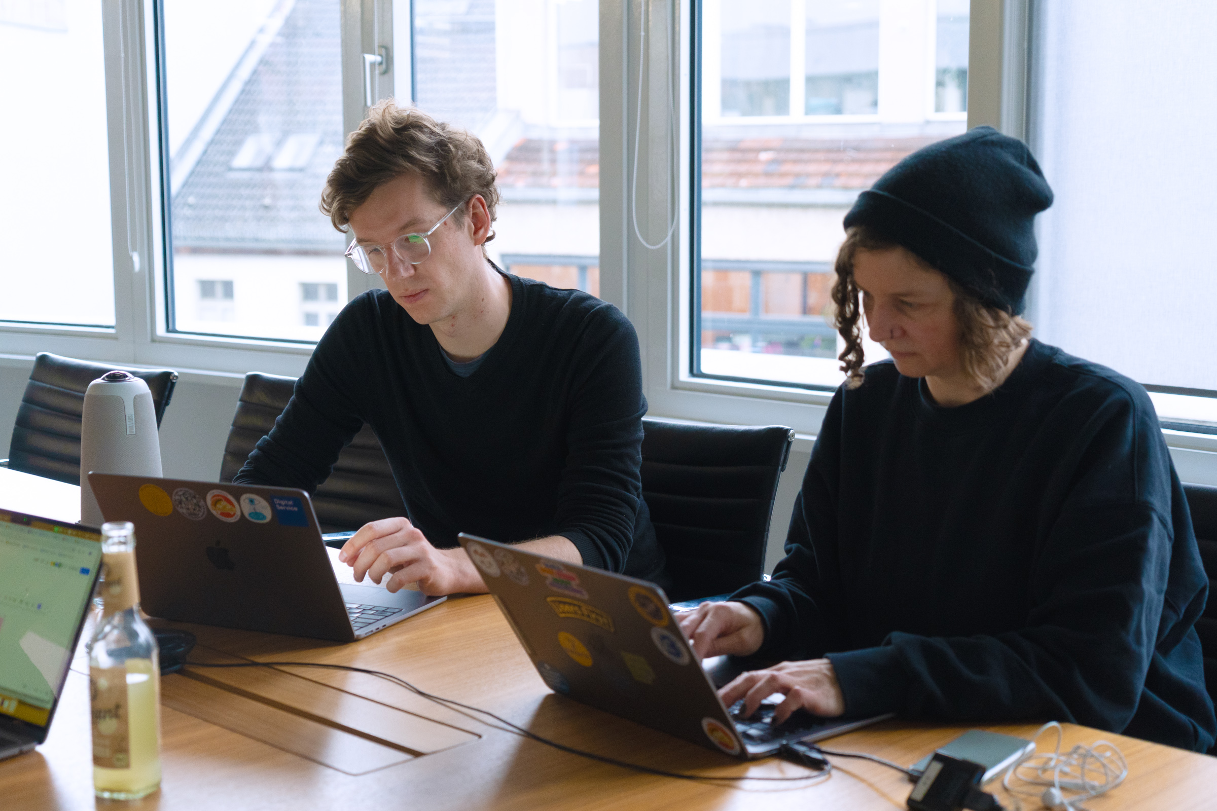 Zwei Teammitglieder der User-Research-Subdisziplin sitzen zusammen an einem Tisch und arbeiten beide an ihren Laptops