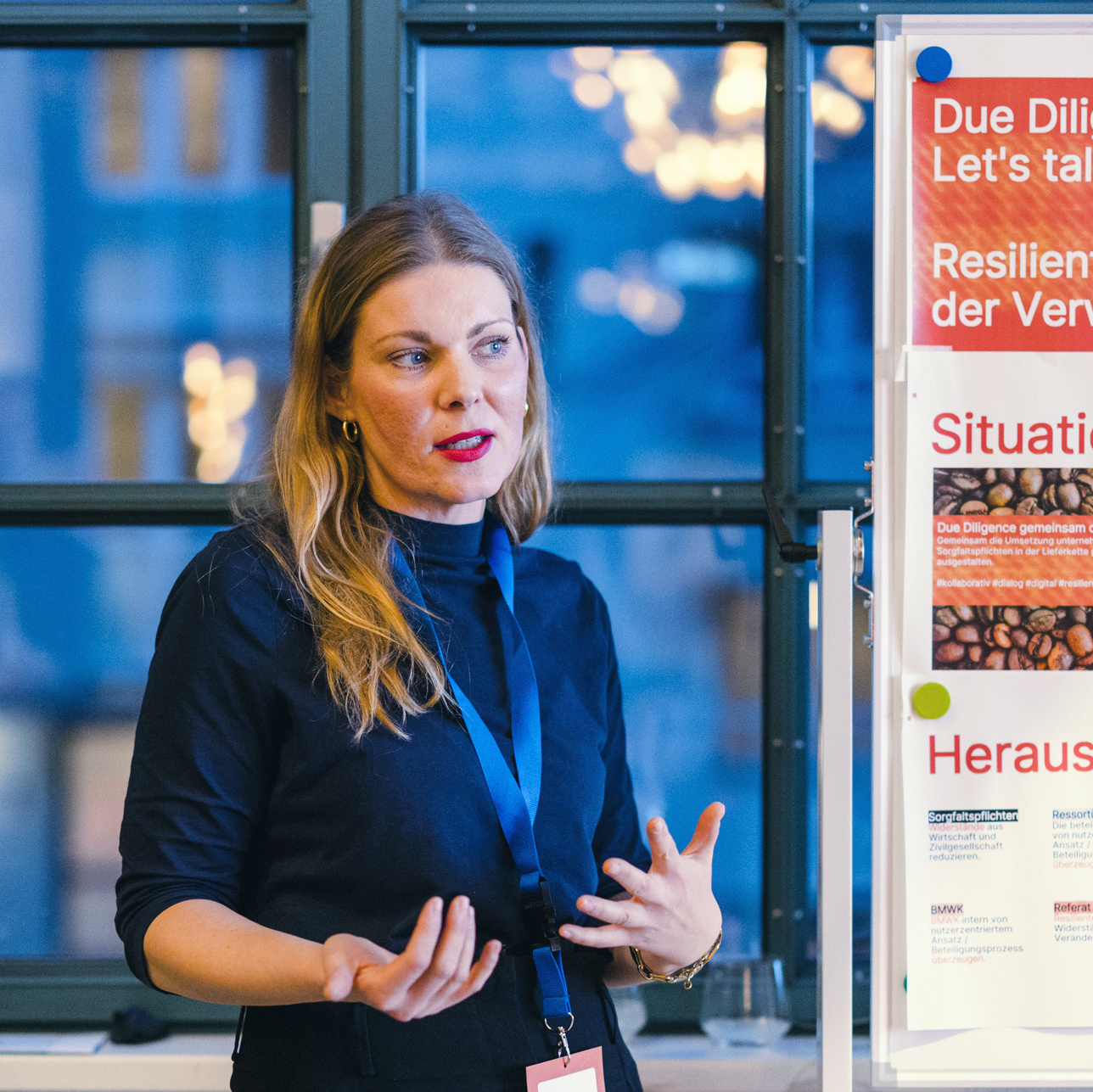 Eine Frau steht neben einem Whiteboard mit verschiedenen Ausdrucken und erklärt diese gestikulierend
