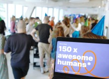 Im Vordergrund ist auf einem Laptopbildschirm zu lesen, dass mehr als 150 Mitarbeitende nun beim DigitalService arbeiten; im Hintergrund sind unscharf zahlreiche Mitarbeitende zu erkennen, die gemeinsam feiern