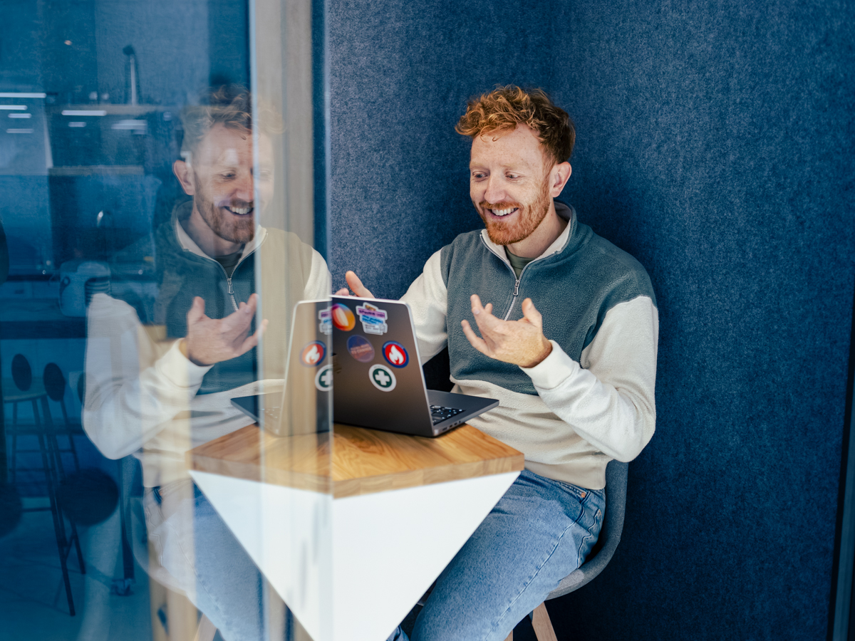 Ein DigitalService Mitarbeitender sitzt in einer Telefonbox und gestikuliert gut gelaunt während er in einem Videocall ist