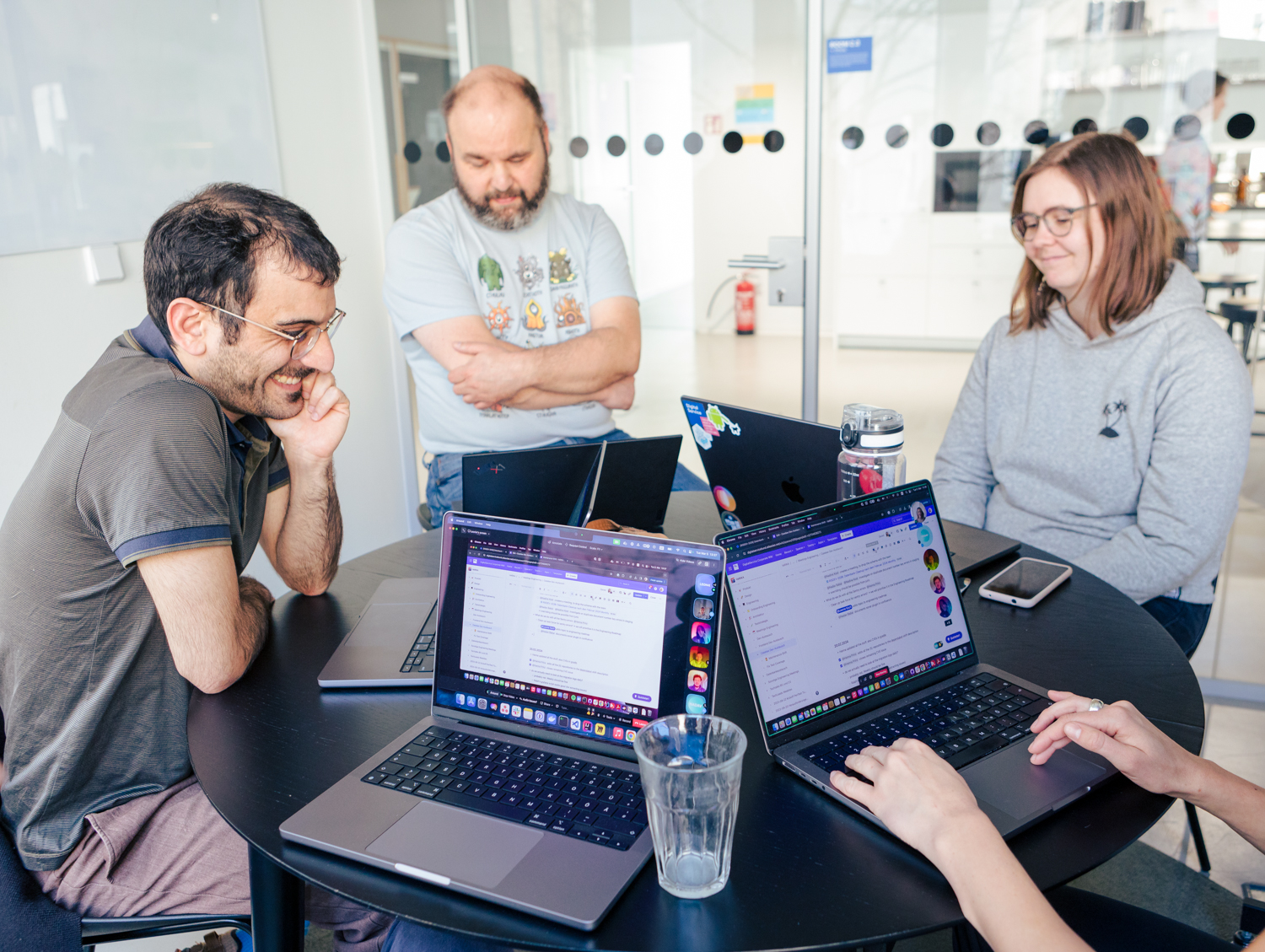 Mitarbeitende des DigitalService sitzen gemeinsam an einem Tisch und arbeiten; sie schauen in ihre Laptops und sind mit anderen virtuell im Austausch